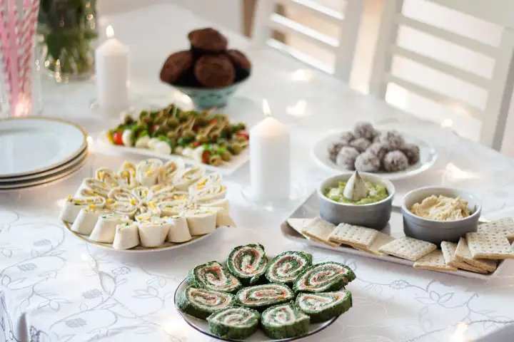 Stół zastawiony pysznymi przystawkami na imprezę domową: roladki z tortilli, szpinakowe roladki z łososiem, mini caprese, kulki czekoladowe i dipy.